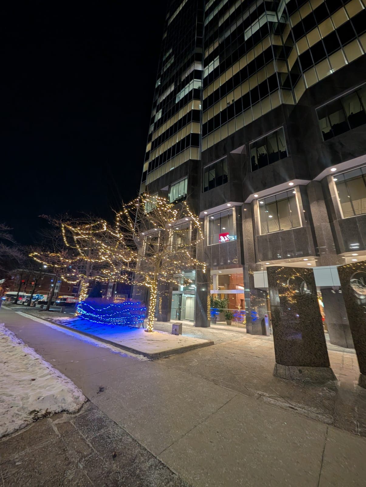 A decorated storefront with warm white Christmas lights and a wreath on the door along a downtown Kitchener commercial street
